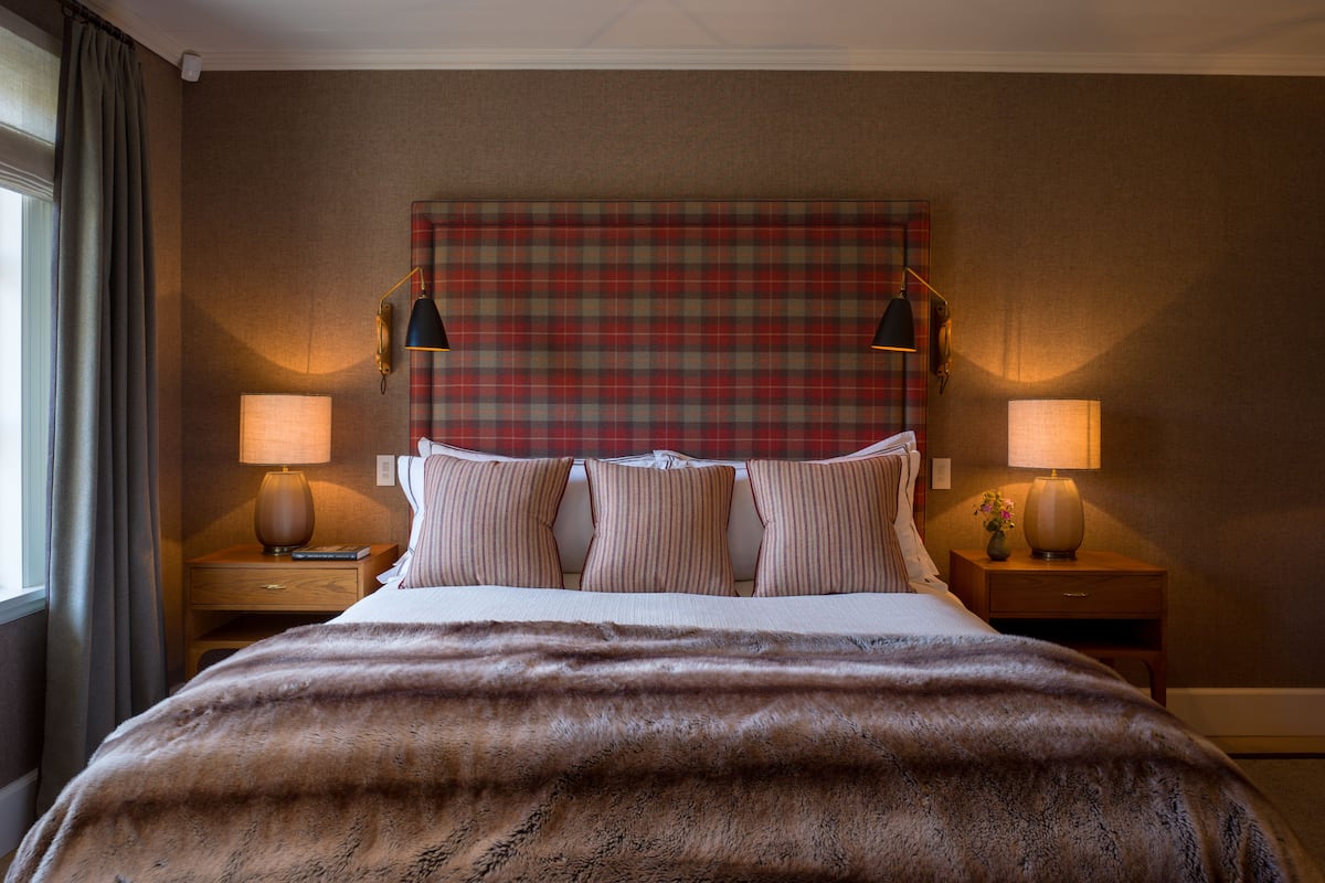 Une chambre d’hôtel avec un grand lit, une tête de lit à carreaux, deux lampes de chevet et un plaid en fausse fourrure.