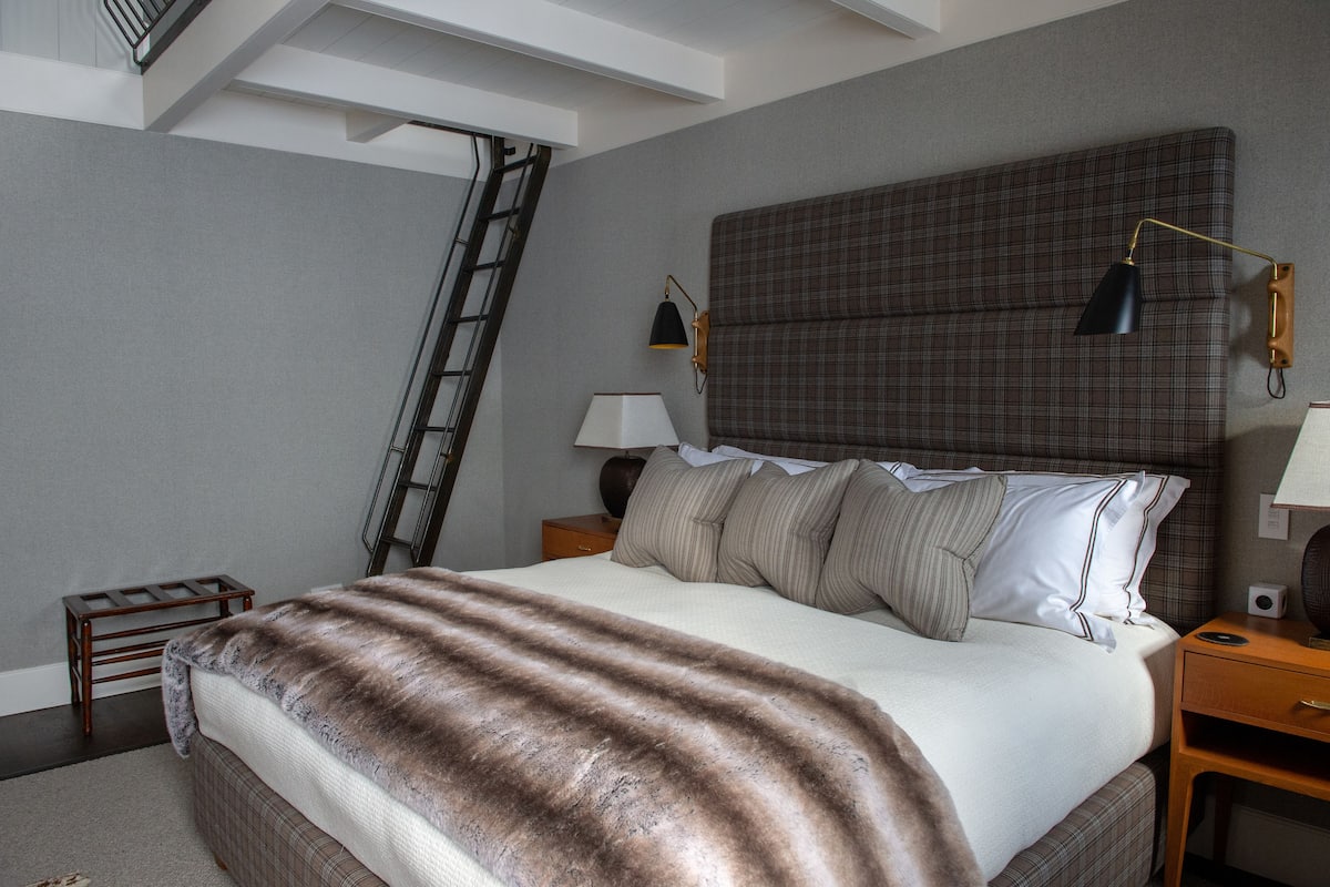Une chambre à coucher avec un grand lit, une tête de lit, deux tables de chevet, une lampe, une échelle et un petit tabouret en bois.