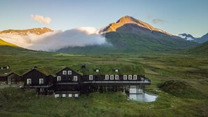 A traditional black wooden house with a thatched roof, situated in a grassy valley with a mountain in the background. - Eleven Deplar Farm - All inclusive (Skagafjörour)