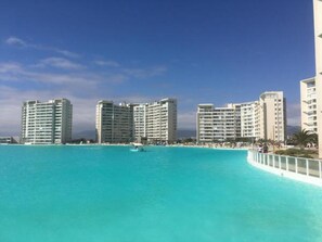 A beachfront hotel with multiple high-rise buildings, a clear blue sea, and a white railing along the shore.