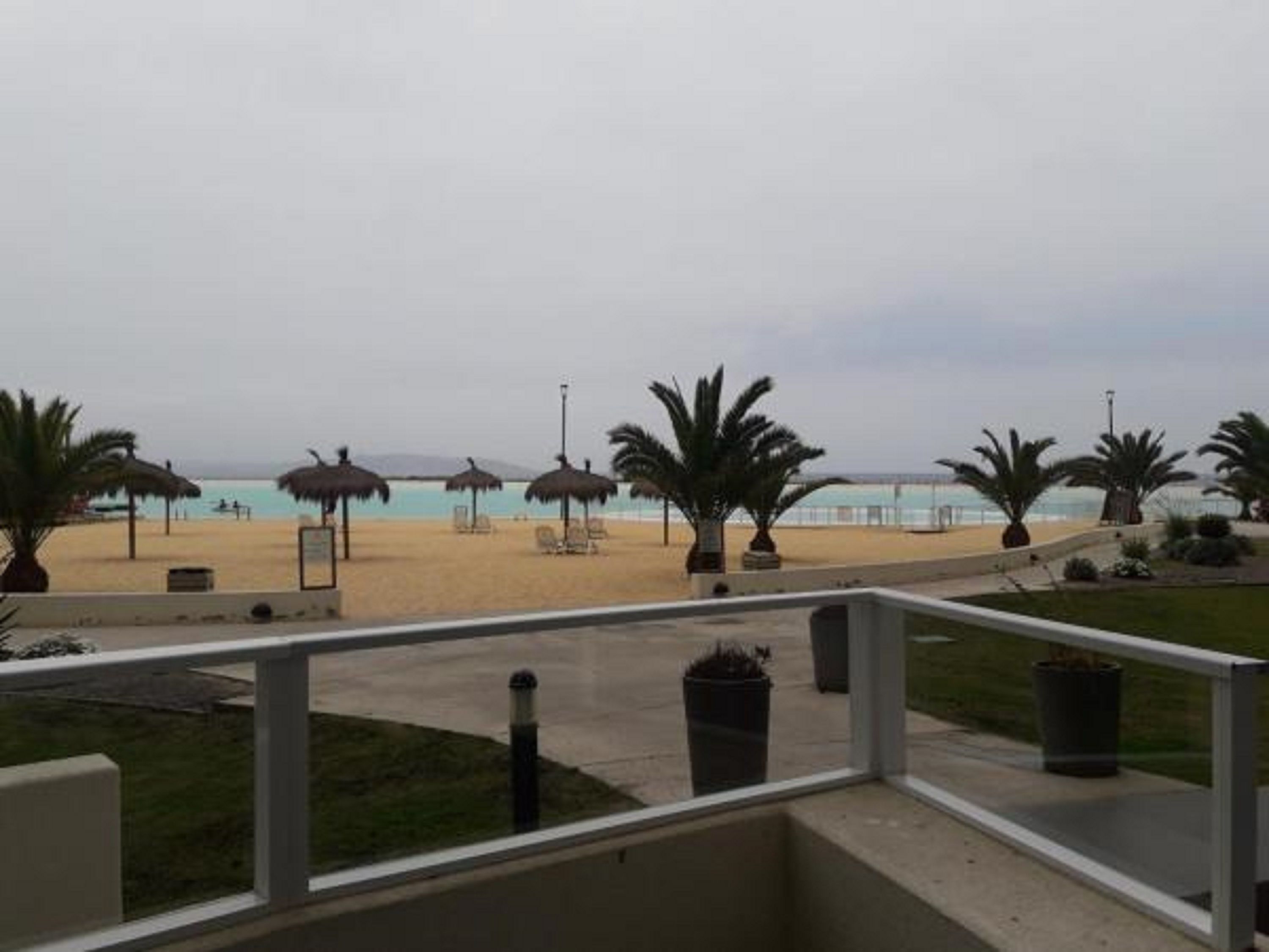 A balcony with a view of a beach, palm trees, and beach umbrellas.