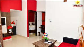 Ein modernes Hotelzimmer mit rotem und weißem Farbschema, einem hölzernen Couchtisch mit Blumenvase, einer schwarzen Couch und einem Bett mit roter Akzentfarbe.