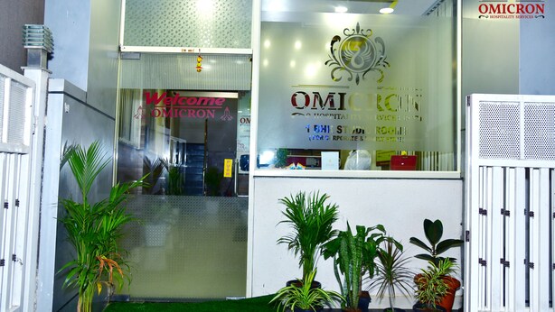 Ein Empfangsbereich mit Glastür, Topfpflanzen und einem Schild mit der Aufschrift 'Welcome Omicron Hospitality Services'.