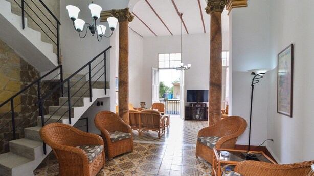A spacious living area with wicker furniture, a staircase, and a view to an outdoor balcony. - Hostal Belvédère (Havana)