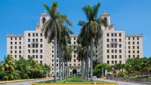 A large, multi-story hotel with a symmetrical facade, palm trees in front, and a clear blue sky. - Hostal Belvédère (Havana)
