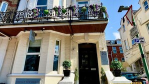 A multi-story building with a prominent entrance, a balcony with decorative plants, and a clear blue sky in the background. - The Hedley Townhouse (Bournemouth)