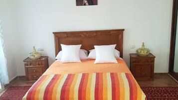 Un dormitorio con una cama de madera, dos mesitas de noche, una lámpara colgante y una alfombra estampada.