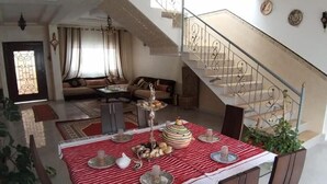 Un comedor con mantel a rayas rojas y blancas, sillas de madera y un elemento decorativo central. Una escalera con barandilla metálica conduce a un nivel superior.