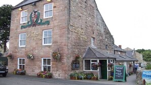 A stone building with "The Craster Arms" signage, featuring a pub and a smaller attached shop.