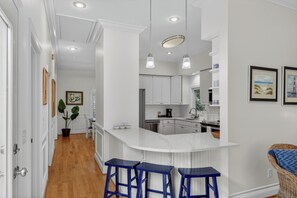 Una cocina moderna con armarios blancos, encimera de mármol y taburetes de bar azules.