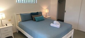 A neatly made bed with a blue bedspread and pillows, a bedside lamp, and a folded towel on the bed. - Cabbage Palm Holiday Home (Agnes Water)