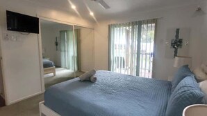Un dormitorio con cama, televisor montado en la pared y ventana con cortinas.