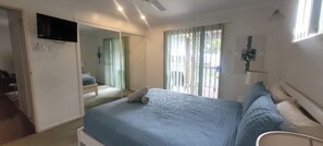 A bedroom with a bed, a TV mounted on the wall, and a window with curtains. - Cabbage Palm Holiday Home (Agnes Water)