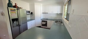A compact kitchen with a refrigerator, microwave, oven, and sink. - Cabbage Palm Holiday Home (Agnes Water)