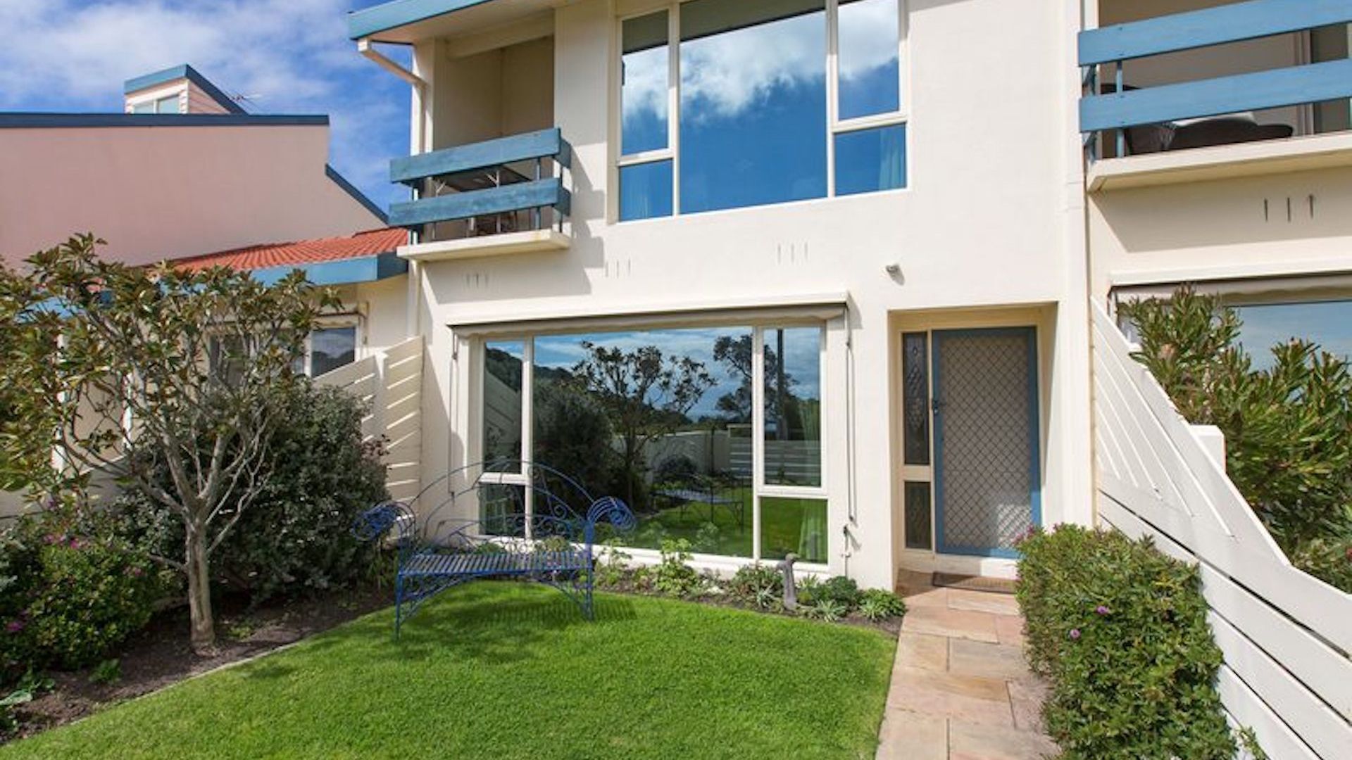 A modern two-story building with a flat roof, large windows, and a small front garden.