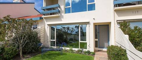 A modern two-story building with a flat roof, large windows, and a small front garden.