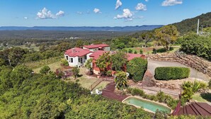 A large, multi-story house with a red roof, surrounded by lush greenery and a swimming pool. - Villa 6 @ Bimbadeen Estate - Spa studio for 2 - Amazing views at every turn (Mount View)