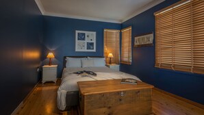 A bedroom with a bed, bedside tables, a wooden chest, and wall art.