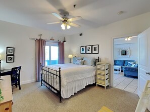 A bedroom with a bed, a ceiling fan, a dresser, a desk, and a chair.