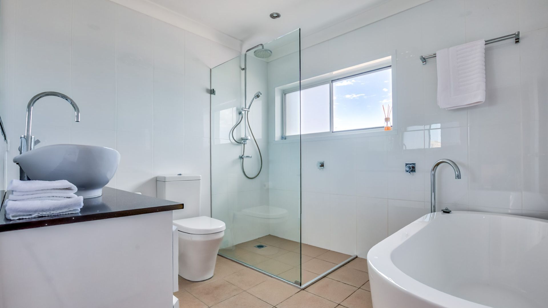A modern bathroom with a glass-enclosed shower, a large bathtub, a sink with a bowl, and a toilet.