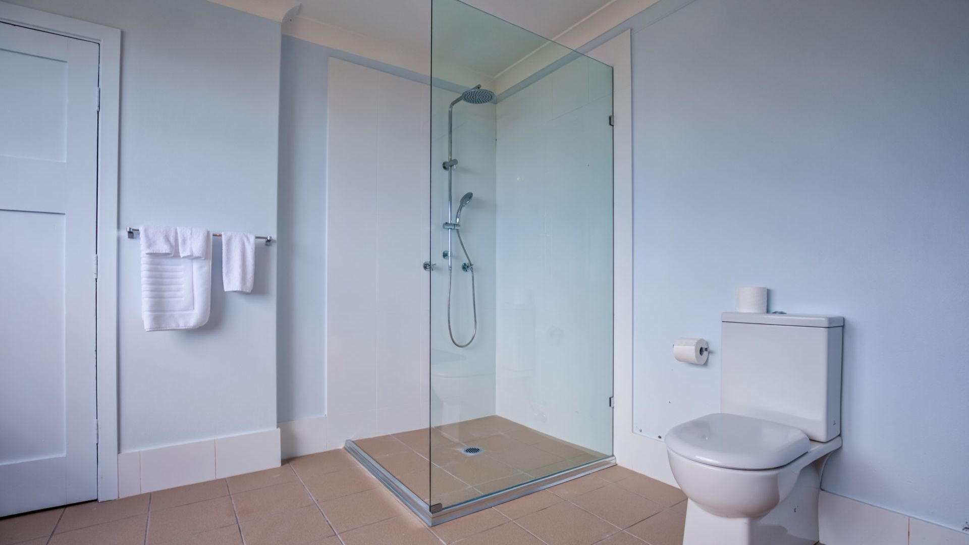 Et moderne badeværelse med en bruseniche, toilet og en håndklæderække med håndklæder.