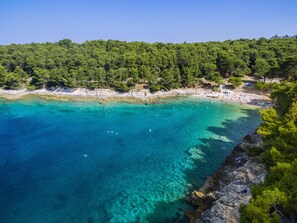 Une zone côtière caractérisée par des eaux turquoise et limpides, une plage de sable et une colline boisée.
