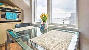 A modern kitchen with a built-in oven and a dining area with a glass table and chairs. - Harbor Views + Private Deck: Waterfront P-Town Apt (Provincetown)