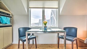 A modern kitchen with a dining table and chairs, a window with blinds, and a vase with flowers on the table. - Harbor Views + Private Deck: Waterfront P-Town Apt (Provincetown)