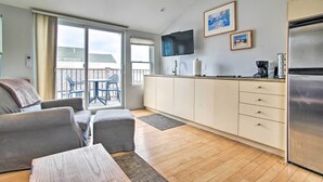 A modern kitchen with a flat-screen TV, a refrigerator, and a dining area with a table and chairs. - Harbor Views + Private Deck: Waterfront P-Town Apt (Provincetown)