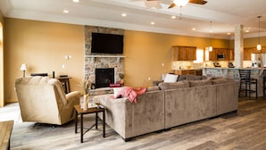 A spacious living room with a large sectional sofa, a fireplace, a television, and a kitchen area with wooden cabinets and a bar. - DRAMATIC LAKEFRONT EAGLES LANDING BREATHTAKING VIEWS (Lake Harmony)