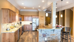 A spacious kitchen with wooden cabinets, a granite countertop, a built-in island, and a stone accent wall. - DRAMATIC LAKEFRONT EAGLES LANDING BREATHTAKING VIEWS (Lake Harmony)