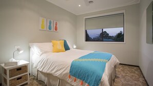 A bedroom with a bed, a bedside table with a lamp, a window with a view, and wall art. - ROANJOKA - DROMANA.... (Dromana)