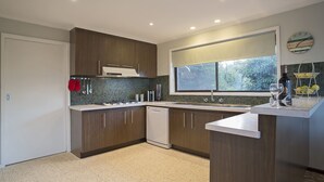 A modern kitchen with dark wood cabinets, a dishwasher, a window with a view, and a wine bottle on the counter. - ROANJOKA - DROMANA.... (Dromana)