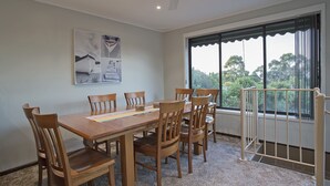 A dining area with a wooden table and chairs, a rug, and a window with a view of trees. - ROANJOKA - DROMANA.... (Dromana)