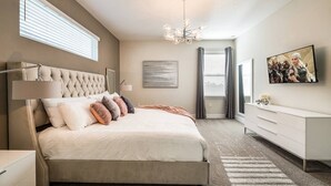 Ein Schlafzimmer mit einem gebürsteten Kopfteil, einem großen Bett, einem Schminktisch, einem Fernseher und einer Kandelaber.