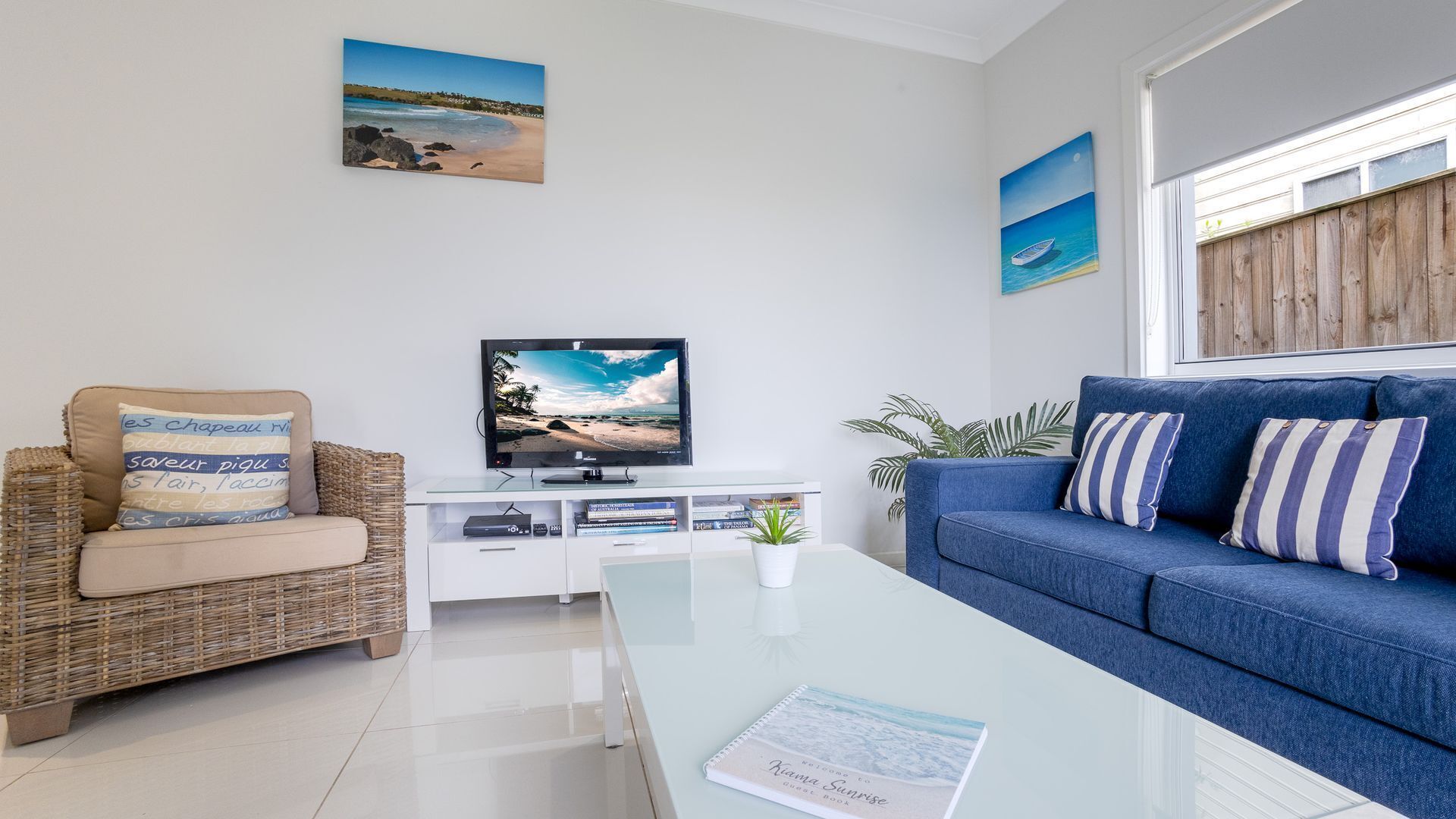 Una sala de estar moderna con una televisión, un sofá azul, una silla de mimbre y una mesa de centro.