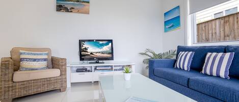 Una sala de estar moderna con una televisión, un sofá azul, una silla de mimbre y una mesa de centro.