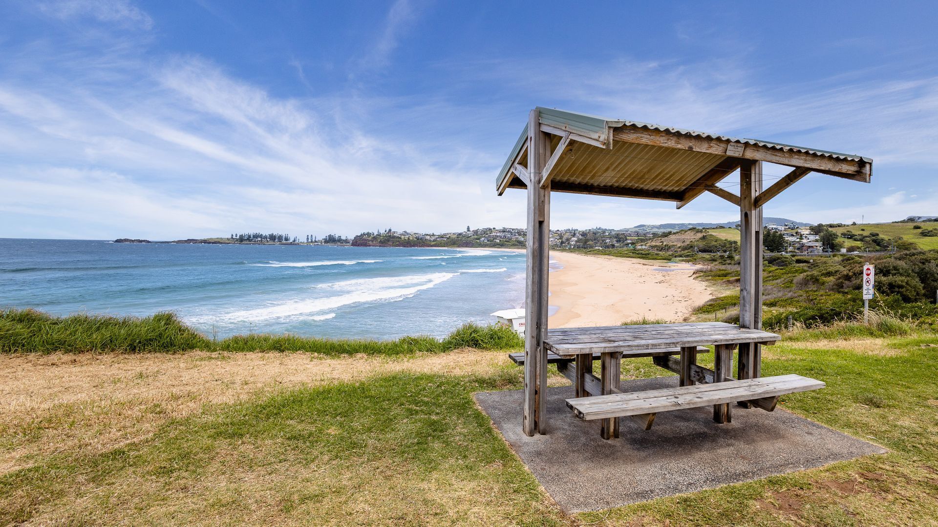A beach with a wooden pavilion and picnic table.