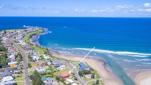 An aerial view of a coastal residential area with houses along the shoreline, a beach, and a clear blue ocean.