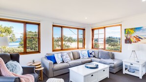 A modern living room with a sectional sofa, a coffee table, and a side table. Large windows provide a view of the outdoors.
