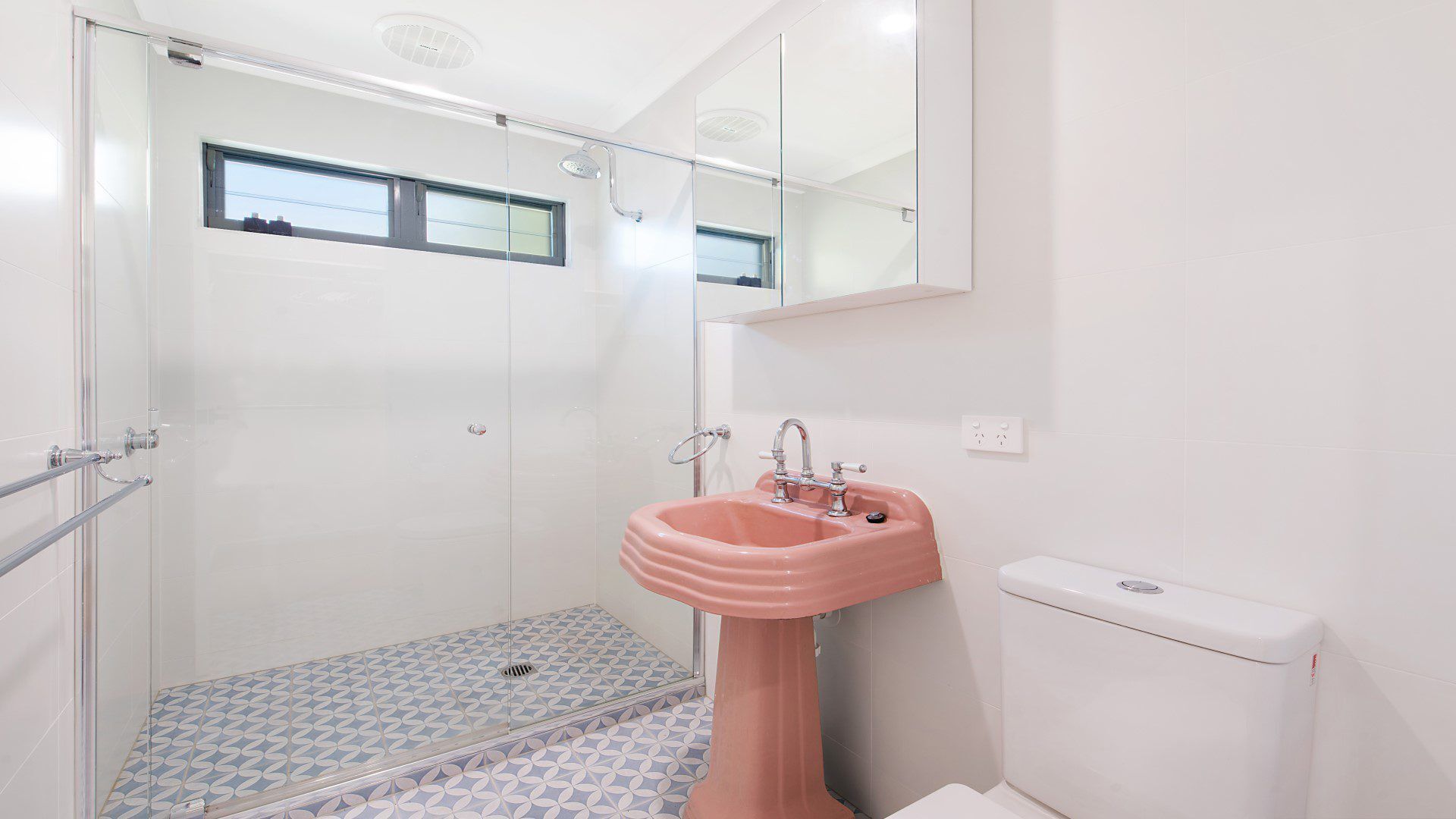 Une salle de bain avec une douche à parois de verre, un lavabo rose et des toilettes.