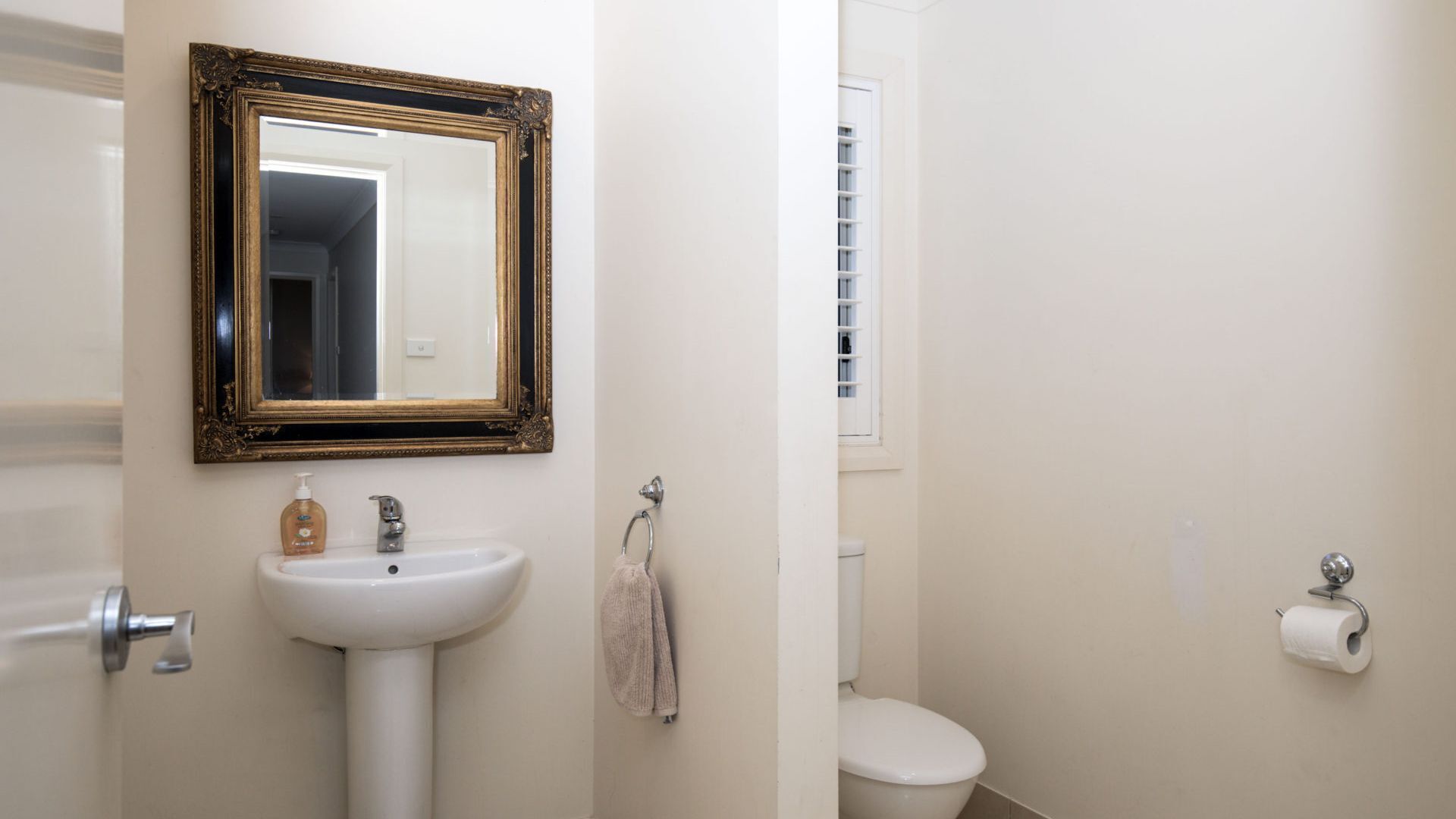Une salle de bain avec un lavabo blanc, un miroir à cadre doré, des toilettes et un rouleau de papier toilette.