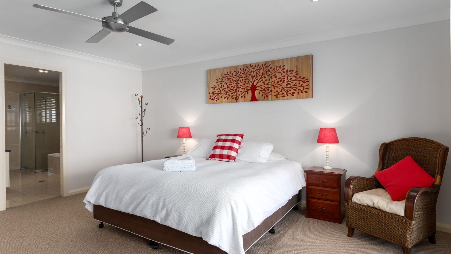 Une chambre à coucher avec un lit, deux tables de chevet avec des lampes, une chaise, un porte-manteau et un tableau accroché au mur.