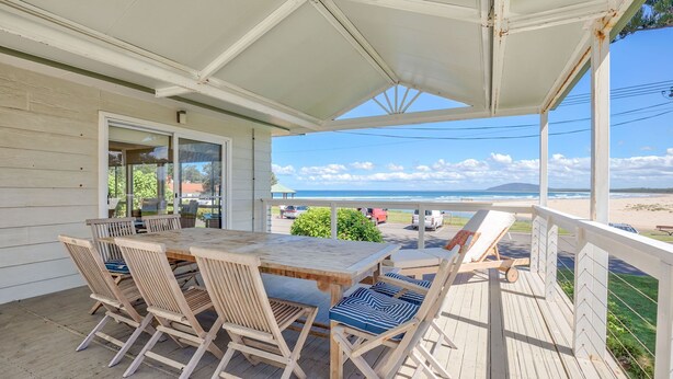 Une terrasse en bois avec une table et des chaises, donnant sur une plage et l’océan.
