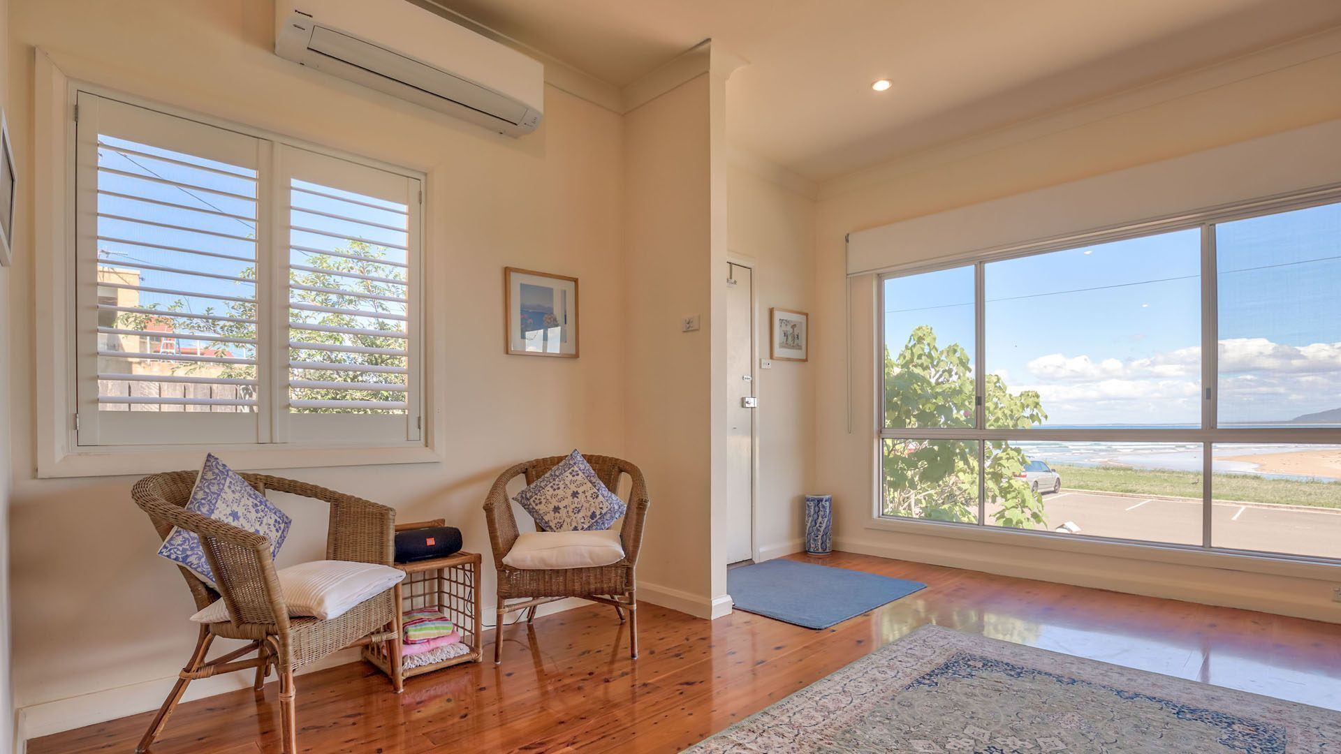 A spacious room with large windows, wicker chairs, a small rug, and a door leading outside.