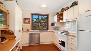 A modern kitchen with white cabinets, stainless steel appliances, a wooden countertop, and a window with a view of trees. - Charming Cottage Retreat by HolidayCo. (KILLCARE)