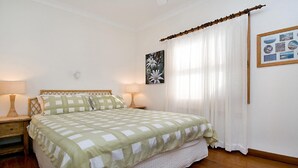 A bedroom with a bed, two bedside lamps, a wall-mounted picture, and a window with sheer curtains. - Charming Cottage Retreat by HolidayCo. (KILLCARE)