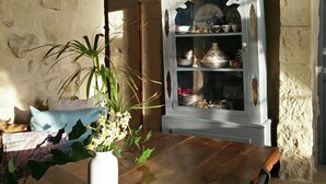 Un interior rústico con una mesa de madera, una planta en maceta y un armario blanco con vajilla.