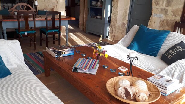 Una sala de estar acogedora con una mesa de centro de madera, un sofá con cojines azules y una estantería llena de libros y objetos decorativos.