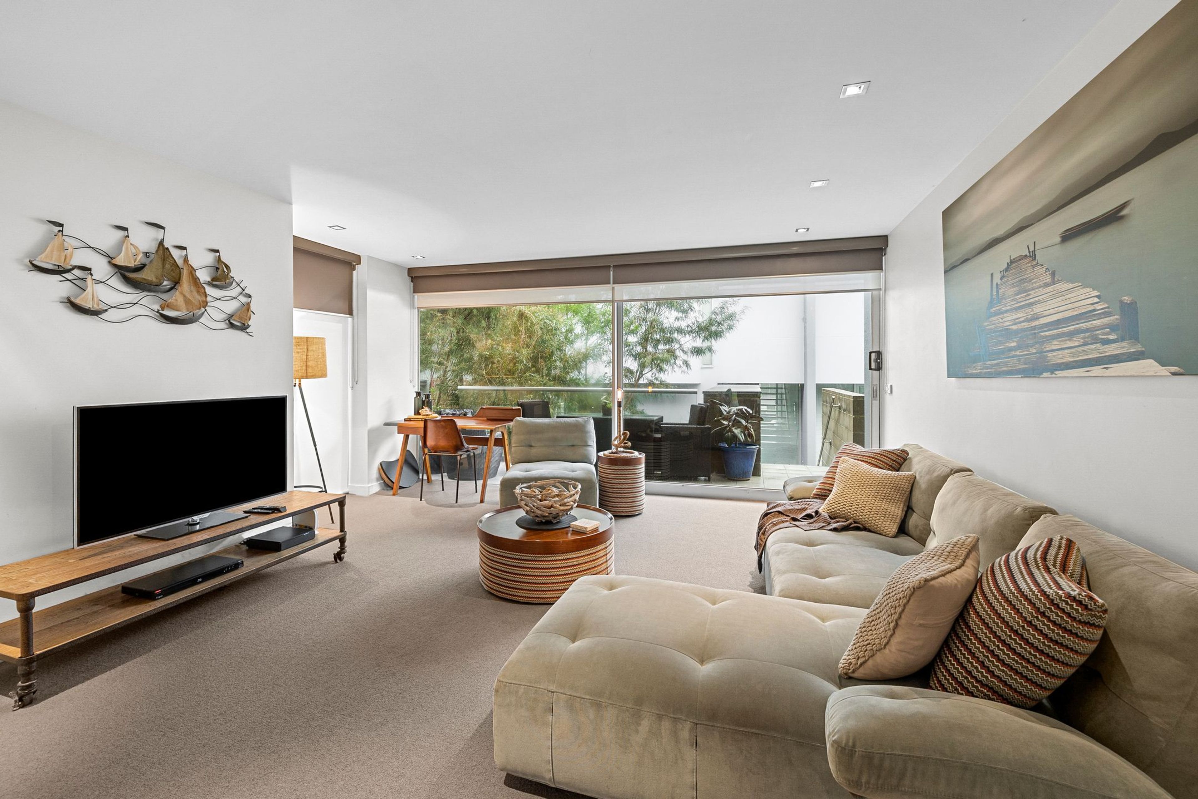 A modern living room with a flat-screen TV, a sofa, a coffee table, and a dining area with a table and chairs.